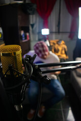 A microphone condenser with a arm, and a guy playing guitat at the background