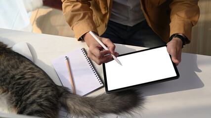 Cropped shot of young man designer working online with digital tablet and cute cat lying next to him.