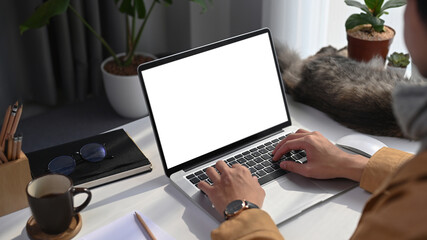 Young man freelancer working online with computer laptop while sitting with his cat at home.