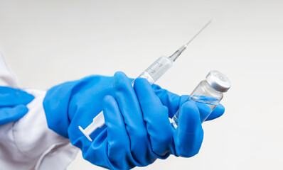 A bottle of COVID-19 vaccine and a syringe with a needle for injections for coronavirus infection in the hand of a doctor in a nitrile glove on a white background. Concept fighting Coronavirus