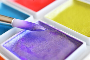 A close up image of a brightly colored set of water color paints with paint brushes.  