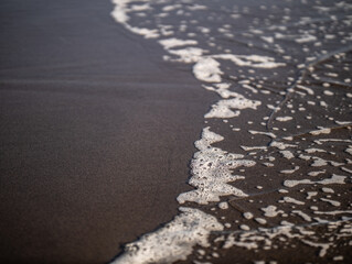 Wave close up on black sand beach. Waterscape background. Selected art focus. Black sand beach with white milky foam waves. Nature and environment concept. Black and white contrast.