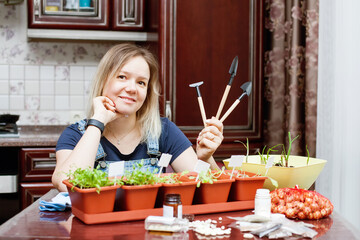 Girl grows seedlings of vegetables and herbs in   kitchen of   house.
