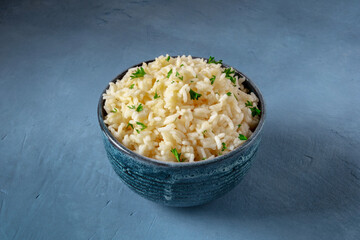 Rice in a bowl on a dark blue background, garnished with fresh parsley leaves