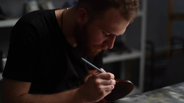 Tracking shot of bearded shoemaker painting heel and sole of light brown leather shoes with brush during restoration working. Process of repairing and restoration shoes by cobbler in shoe repair shop