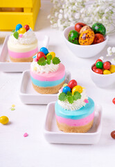 Multicolored mini cheesecakes with candy eggs and whipped cream. Pastel colored Easter dessert