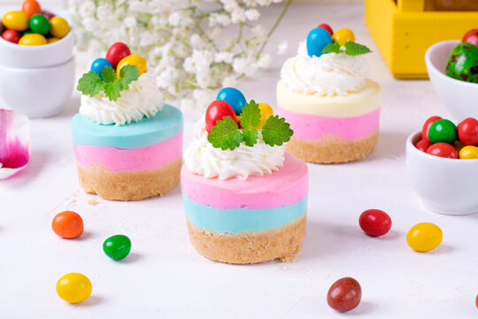 Multicolored mini cheesecakes with candy eggs and whipped cream. Pastel colored Easter dessert