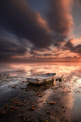 Old fisherman boat. Seascape. Fishing boat at the beach during sunrise. Low tide. Water reflection. Cloudy sky. Slow shutter speed. Soft focus. Sanur beach, Bali.