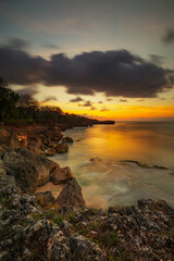 Sunset view. Seascape background. Amazing ocean view. Beach with rocks and stones. Bright sunlight on horizon line. Cloudy sky. Vertical layout. Bali.