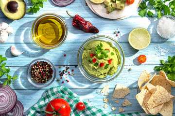 Bowl of guacamole and ingredients on blue background. Top view.