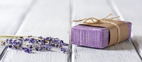 Natural handmade lavender soap with dried lavender flowers on a white wooden table, banner. Side view.