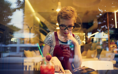 women in a sundress sitting in a cafe and looking at the street through the glass