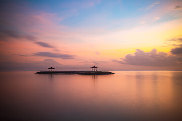 Pink sunrise. Seascape background. Traditional gazebos on an artificial island in the ocean. Water reflection. Calm water surface. Soft focus. Copy space. Sanur beach, Bali.