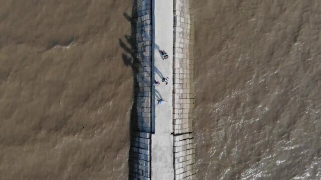 Aerial drone shot of people walking along slowly on a long bridge. Top view of people walking between lake or river with low current and polluted water. Blue boat parking on the side.
