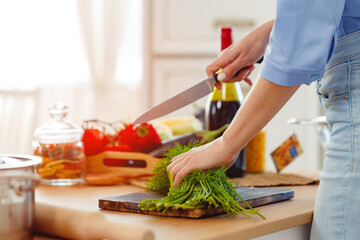 Woman cutting parsley on wooden board in kitchen