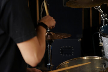 The drummer sits at the drum set and plays. Holds drumsticks in his hands