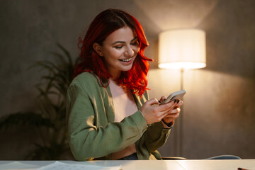 Smiling woman with red hair using mobile phone while sitting at table