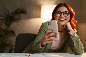 Smiling woman with red hair using mobile phone while sitting at table