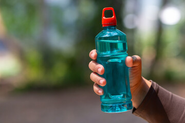 Naklejka premium Clear blue green water bottle, the lid is red with a hole in the center for portability, natural background. With the hand held Drinking with vitamins Drink water in summer Leave space for the text.