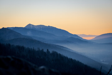 The ridges of Tatra Mountains illuminated by the setting sun. The fog in the valley is covering Zakopane town, Poland. Selective focus on the silhouette, blurred background.