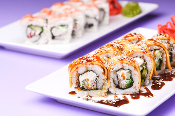 Eel, salmon and tuna sushi with unagi sauce served on a white plate over purple background.