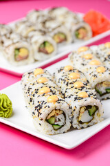 Sushi large set served on a white plate over pink background. Traditional Asian Japanese cuisine concept.