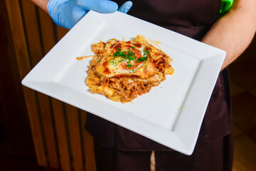 One piece of Lasagna bolognese served by waiter in restaurant or diner. Dinner, eating out concept.