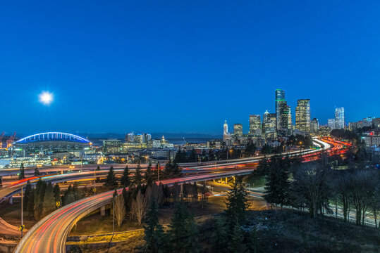 The city skyline of Seattle at night, road and bridge, downtown buildings lit up in moonlight.