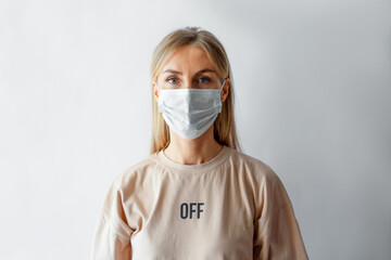 Close-up portrait on a pale background of a caucasian woman in a protective medical mask.