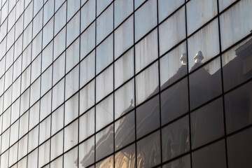 A building with an old architecture is reflected on the geometric mirrored glass of an office building with a modern architecture. Architectural concept from the urban environment