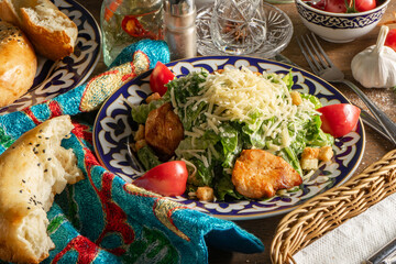 Caesar salad with chicken, tomatoes and cheese in a plate with an Uzbek pattern