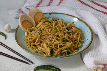 Asian fried noodles with shredded chicken, chilies, spices and boiled egg served on a blue plate over the marble background