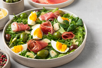 Salad with prosciutto, parmesan, olives, eggs and arugula in a plate on a dark background. Italian appetizer. close up
