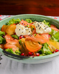 Delicious healthy salmon salad with cheese and pomegranate seeds served in a bowl over traditional Ukrainian tablecloth.