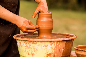 Hands of potter make ceramic jar on pottery wheel outdoor, selective focus