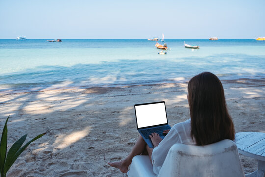Mockup image of a woman using and typing on laptop computer with blank desktop screen while sitting on the beach