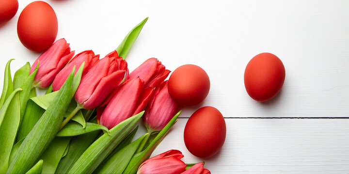 Easter Eggs And Red Flowers On White Wooden Table, Top View. Painted Chicken Eggs And Red Tulip