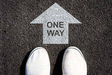 One way. Success. Right direction. White arrow on the road, and sneakers. View from above.