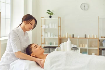Wall murals Massage parlor Good looking female client getting face and neck massage lying on bed in beauty parlor