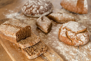 Different loafs of bread on a wooden table with flour surrounding the bread.  Whole wheat and whole grain perfect for a bakery.