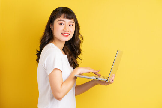 Young Asian Woman Holding Laptop On Yellow Background