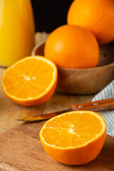 Top view of half orange, knife and unfocused oranges on wooden table, black background, vertical
