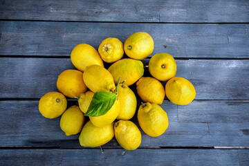 Group of  lemons with one bearing a leaf on a wood table
