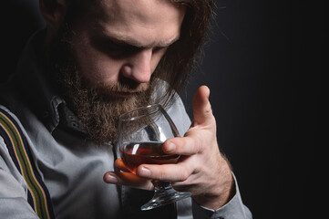 Man with beard holds glass brandy. Bearded drink cognac. Sommelier tastes drink. Man holding a...