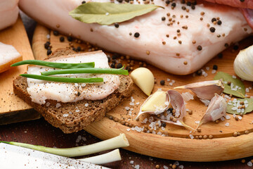 raw pork meat and lard with salt, spices and garlic on a cutting board, dark wooden background