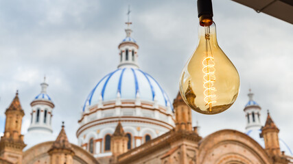 Cathedral of immaculate conception, blurred in the background, also known in spanish as Catedral Nueva, Cuenca, Ecuador. In the foreground a light bulb.