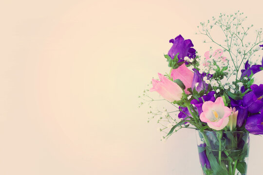 spring bouquet of purple, white and pink bell flowers over purple wooden background