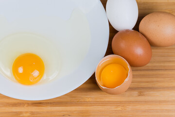 Whole and broken eggs on dish, top view close-up