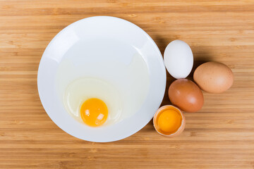 Whole and broken eggs on dish on a wooden surface