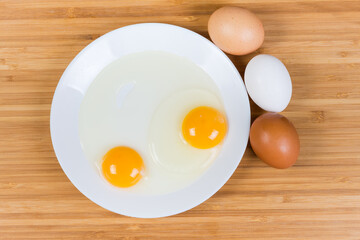 Broken eggs on dish and whole eggs beside, top view